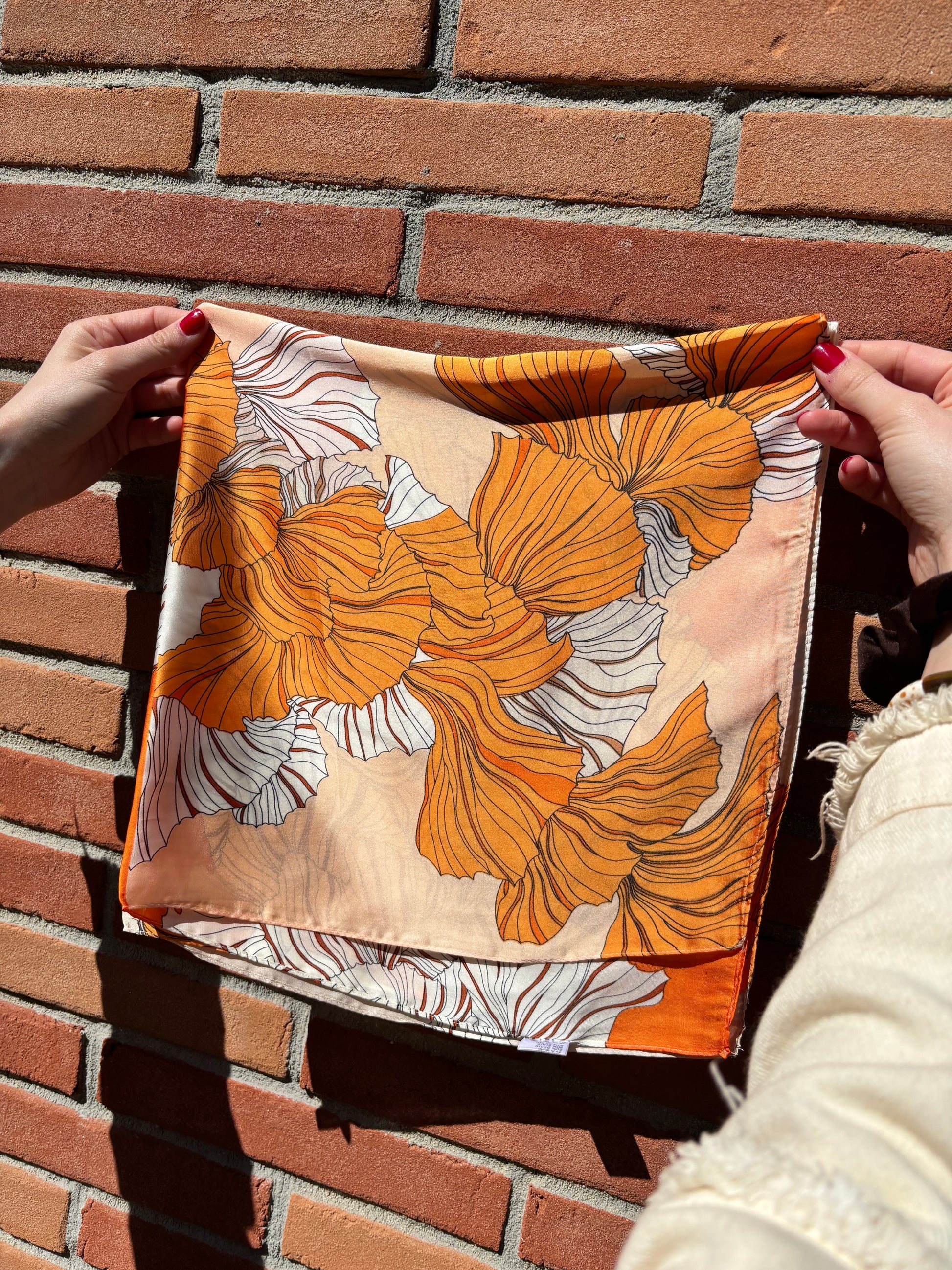 Foulard en soie léger décoré de fleurs orange et blanches, parfait pour un style à la fois sophistiqué et actuel.